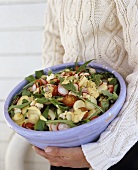 Person holding bowl of potato and rocket salad