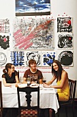 Three young people at dining table below modern artworks on wall