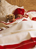 Mädchen mit Mütze und Teddybär unter einer Wolldecke