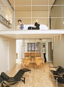 Man in open-plan kitchen, woman lying in front of sofa on mezzanine above