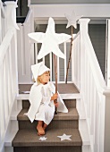 A girl sitting on a flight of stairs holding a Christmas star