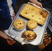 Frau hebt Backblech mit verschiedenen Pies aus dem Backofen