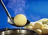 Potato dumpling being lifted out of pan on skimmer