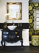Eine schwarz lackierte Barockkommode dient mit einem modernen Becken als Waschtisch und wird stilistisch durch einen goldenen Spiegel ergänzt