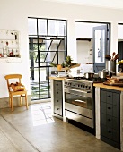 Kleine Küchentheke mit Edelstahlherd vor Terrassentür und Fabrikfenster