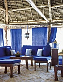 Blaue Loungemöbel und Vorhänge in einem Strandpavillon mit traditioneller Holz- und Strohkonstruktion