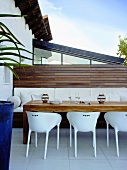 weiße Schalenstühle und Polsterbank an einem schön gemaserten Holztisch auf der Dachterrasse