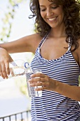 Junge Frau giesst Mineralwasser in ein Glas