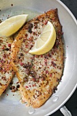 A fried peppered plaice with two lemon wedges