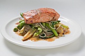 A fried salmon fillet on mie noodles and vegetables