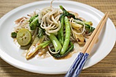A plate of noodles and vegetables with chopsticks