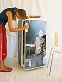 Mädchen schaut in einen mit Fotomotiv dekorierten Kühlschrank
