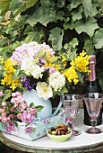 Jug of flowers, sparkling wine and glasses on garden table