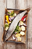 Hake with vegetables, lemons and parsley on a baking tray