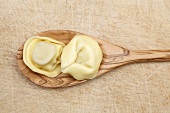 Two cooked tortellini on a wooden spoon