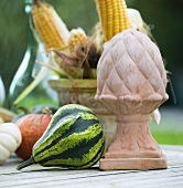 Ornamental pumpkins, a terracotta statue and corn cobs on a garden table