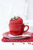 A strawberry-shaped candle in a red espresso cup