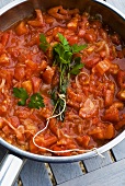 Tomato sauce with bunch of herbs in pan