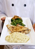 Chef serving veal escalopes with risotto and vegetables