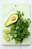 Half an avocado, coriander and lime wedges on white board