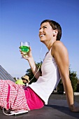 Young woman drinking cocktail & listening to music on headphones