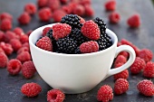 Blackberries and raspberries in and around a cup