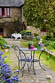 Gartenstuhl & Gartentisch mit Blumen auf gepflastertem Weg zum Haus