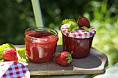 Two jars of strawberry jam & fresh strawberries on chopping board