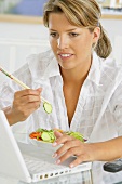 Frau isst Gemüsesalat mit Essstäbchen vor Laptop