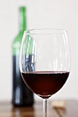 Ein Glas Rotwein, im Hintergrund Rotweinflasche