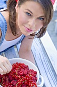 Young woman holding bowl of redcurrants and raspberries