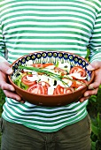 Person holding bowl of salad: tomatoes, egg, lettuce and chives
