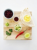 Tortilla and various ingredients on chopping board (overhead view)