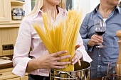 Frau gibt Spaghetti in Kochtopf, daneben Mann mit Rotweinglas