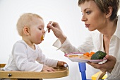 Mother feeding small child with carrot puree