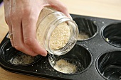 Sprinkling a muffin tin with breadcrumbs