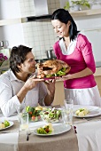 Woman serving roast turkey, man sitting at table