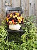 Autumn flowers in hollowed-out pumpkin on a garden chair