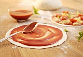Spreading pizza dough with tomato sauce