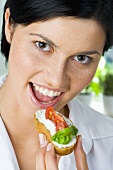 Young woman eating bread topped with soft cheese, tomatoes & basil
