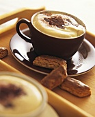 A cup of cappuccino with chocolate shavings and biscuits