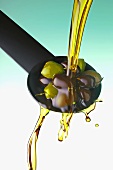 Olivenöl auf Löffel mit Oliven gießen