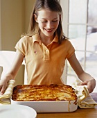 Girl holding vegetable lasagne in baking dish