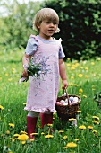 Kleines Mädchen hält Blumen und Korb mit Ostereiern