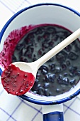 Blackcurrant jam in an enamel pot with a wooden spoon