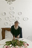 Woman with flowers on a table and white plates on the wall