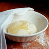 A ball of yeast dough drizzled with olive oil in a bowl covered with a cloth