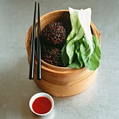 Sesame seed and rice balls with bok choy in a bamboo steamer