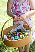 Girl holding a basket of colourful cupcakes