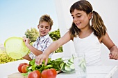 Mädchen und Junge bereiten Salat im Freien zu